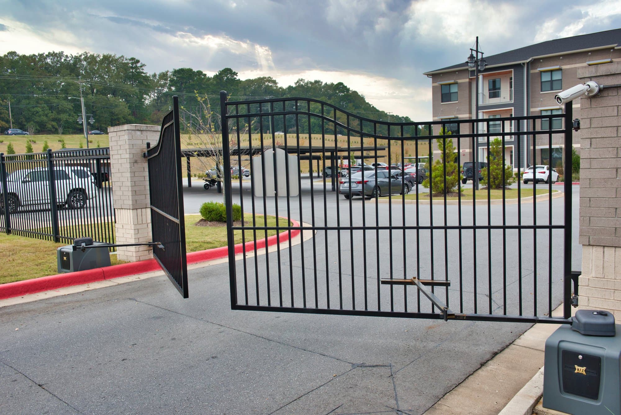 Swing gate open at a multifamily property with parking and building visible