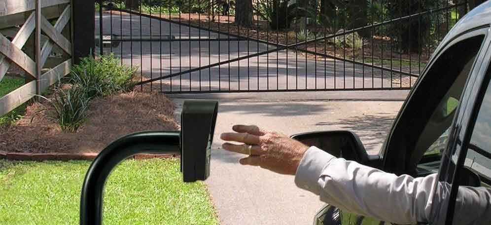 Driver reaching toward a wall-mounted access panel at an open gate